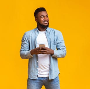 Handsome black man holding smartphone and looking aside at copy space on yellow studio background