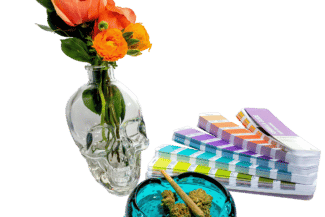 pantone swatches nest to clear skull vase holding flowers by a blue glass ashtray holding cannabis flower and joint