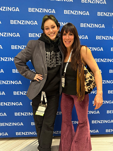 SJ Gringas and Jen Lamboy from Hybrid Marketing Co. smile together at the Benzinga Cannabis Event, posing in front of a branded backdrop.